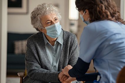 An in home provider talks to a patient in a surgical face mask